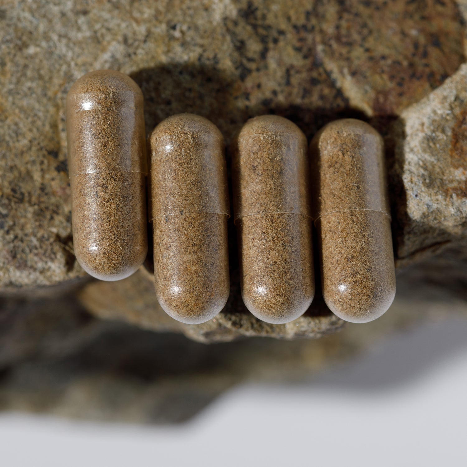 Four Mother of All Prenatals capsules by Wild Mamas rest on a textured rock with another rock above, the blurred background drawing attention to the capsules and rocks for a focus on pure whole food prenatal nutrition.