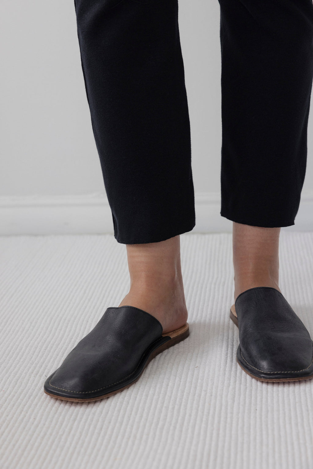 A person wearing Wol Hide's Easy Legging in Black stands on a light-colored carpet, with only the lower legs and feet visible.