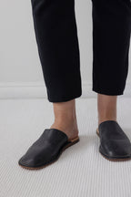 A person wearing Wol Hide's Easy Legging in Black stands on a light-colored carpet, with only the lower legs and feet visible.
