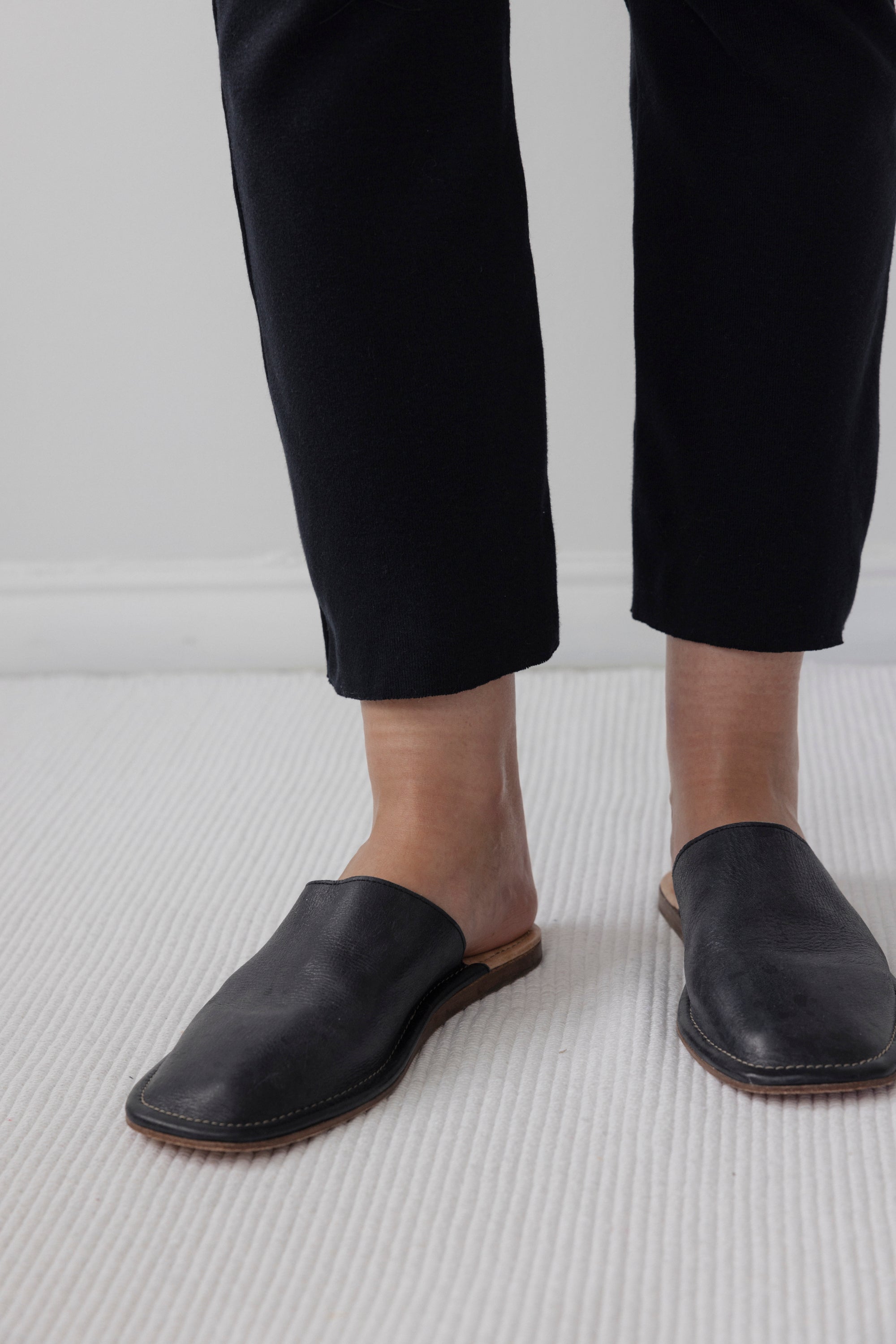 A person wearing Wol Hide's Easy Legging in Black stands on a light-colored carpet, with only the lower legs and feet visible.