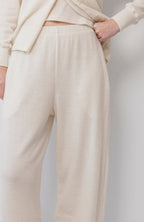 A person wears Wol Hide's Wool Wide Leg: Natural pants—cream-colored, wide leg with an elastic waist—paired with a matching top. The visible lower torso and upper legs highlight the outfit's soft, comfortable look. One hand rests on their hip.