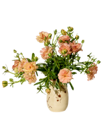 The Baile Homestead Vase by Baile, a cream-colored handmade ceramic piece with small floral details, holds light pink ranunculus and green foliage against a white background.