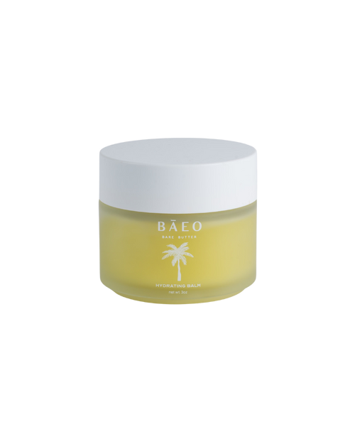 A small frosted glass jar with a white lid holds yellow organic hydrating balm for dry or sensitive skin. The label reads "bare butter" by bāeo and has a palm tree graphic on the front.