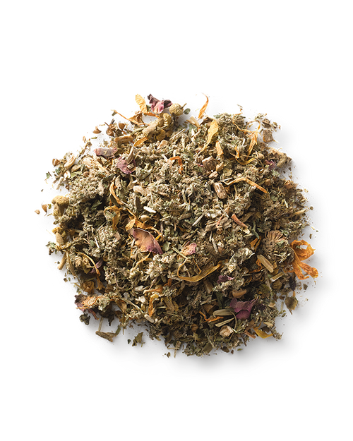 A small, clear glass bowl filled with Surya’s (y)oni Fertility Steam, a mix of dried Ayurvedic herbs and flowers. The blend features various shades of green, brown, and hints of pink and orange petals—an ideal preparation for pregnancy. The bowl is set against a white background.