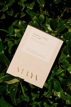 A cream-colored box labeled "Hormone Soothing Bath Soak" by Surya, 27 oz (1.68 lb/0.77 kg), rests on lush green leaves, with product details shown on the packaging.