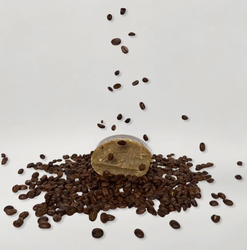 Decaf coffee beans spill from a small container onto a white background, echoing the pure simplicity of Wild Mamas’ Shilajit + Decaffeinated Coffee Bean Deeply Exfoliating Wild Bison Tallow Soap Scrub.