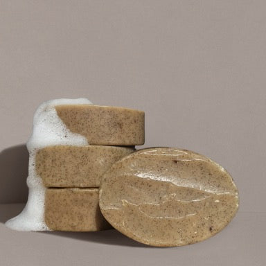 Four oval brown Wild Mamas "Madagascar Vanilla Bean + Manuka Honey" Wild Bison Tallow Soap Scrub bars, made with organic ingredients, three stacked with white foam and one in front, set against a plain light grey background.