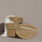 Four oval brown Wild Mamas "Madagascar Vanilla Bean + Manuka Honey" Wild Bison Tallow Soap Scrub bars, made with organic ingredients, three stacked with white foam and one in front, set against a plain light grey background.