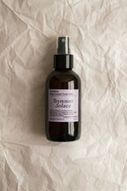 A dark spray bottle labeled "Summer Solace Tallow Lavender & White Lotus Toner – Organic Floral Mist" rests on crumpled, off-white paper. The label includes product details and an Oakland, CA address.