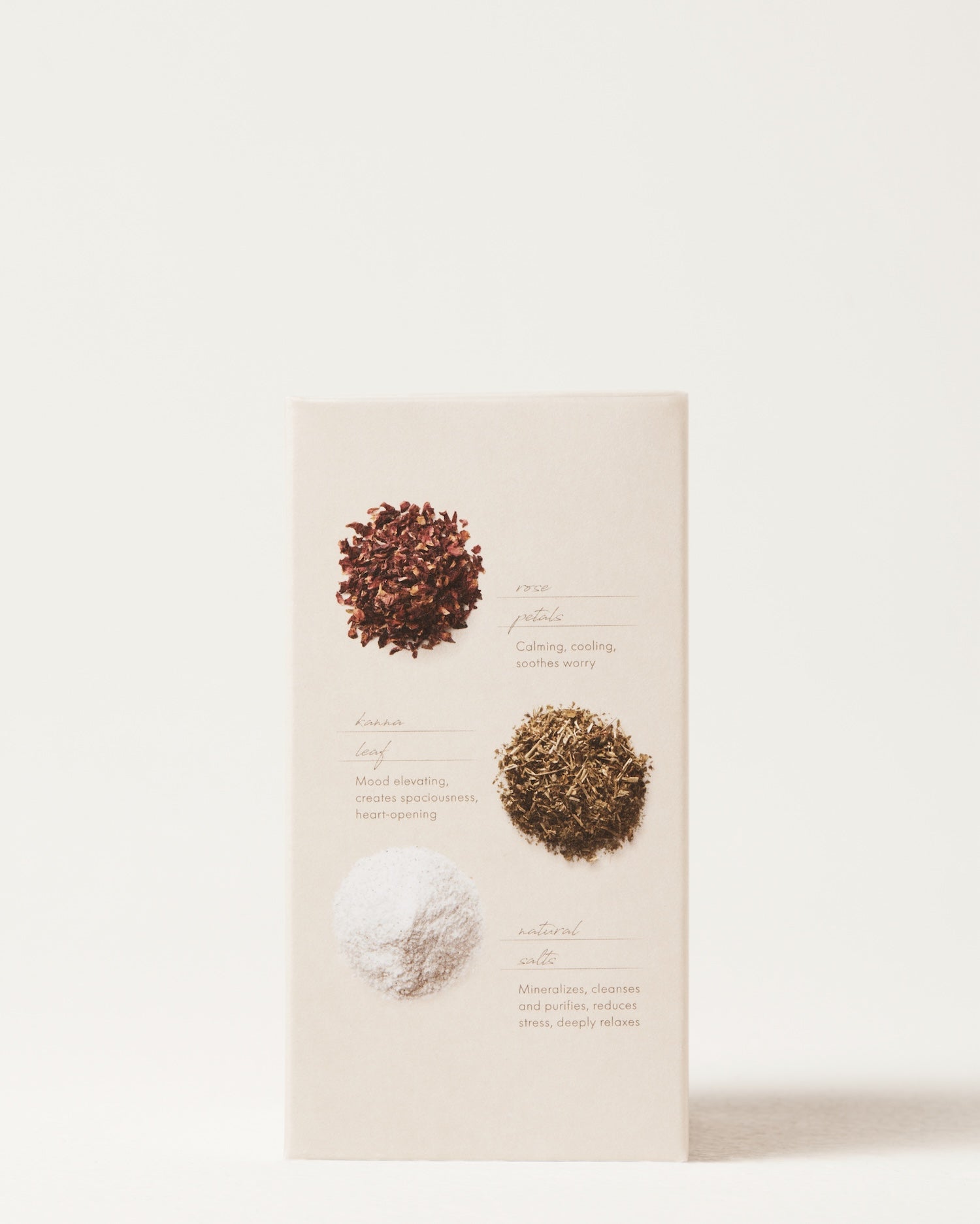 A minimalist box of Surya’s Love Bath Heart-Opening Soak displays three small piles: delicate rose petals (“root”), kanna leaf (“leaves”), and white mineral salt—each shown with a brief description, perfect for a heart-opening bath experience.
