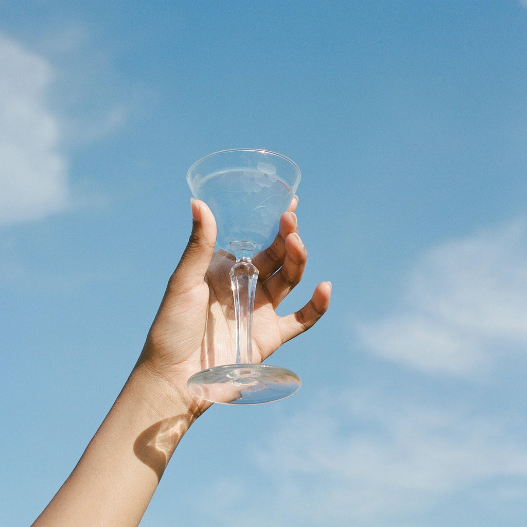 A hand holds up a Magic Magnesium bottle from WOODEN SPOON HERBS against a calm, clear blue sky with wispy clouds, evoking energy and tranquility.