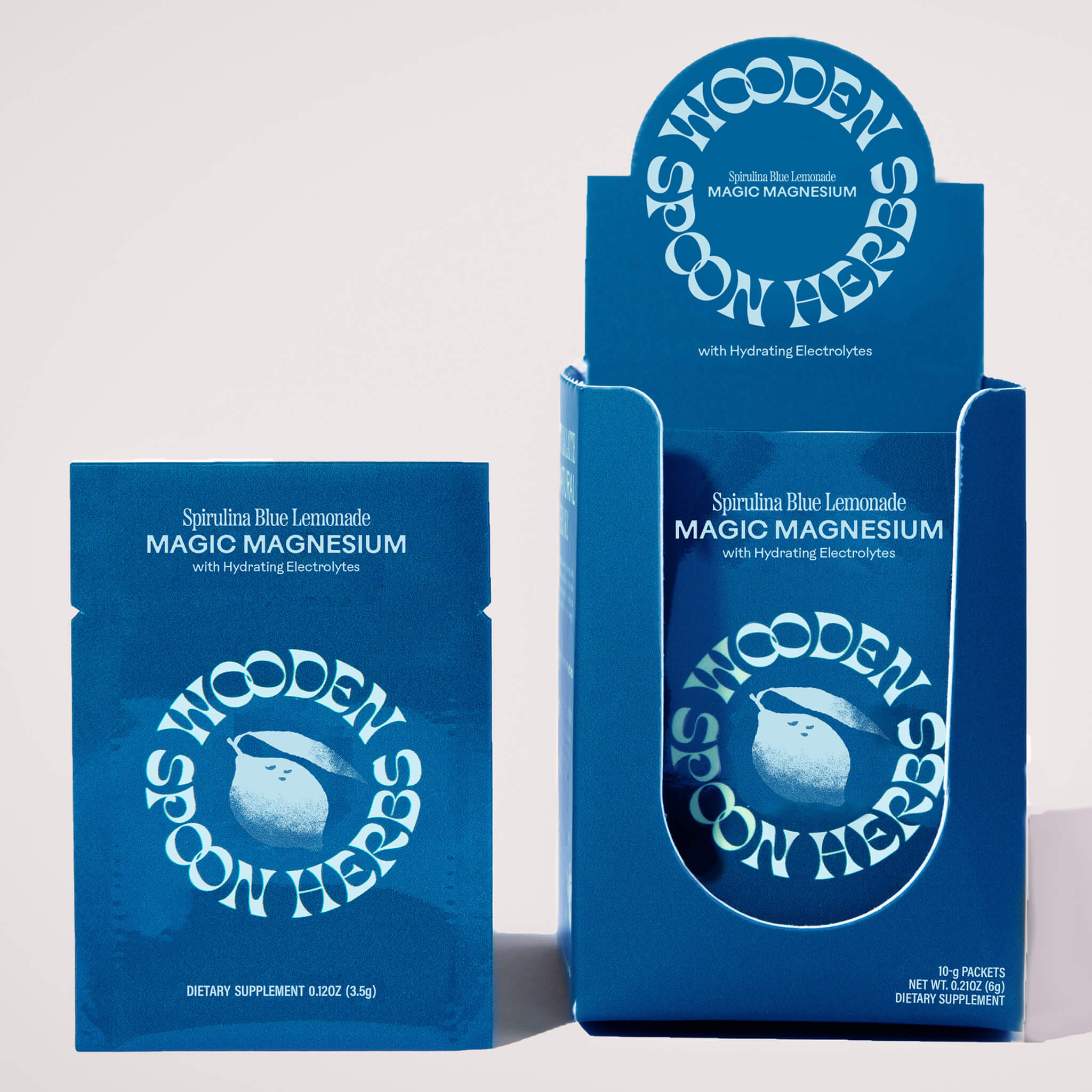A packet and open box of WOODEN SPOON HERBS Magic Magnesium, both in blue packaging with a spoon logo—formulated for calm and energy.