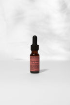 A small amber glass dropper bottle labeled "Summer Solace Tallow" stands upright on a light surface, displaying the limited edition Mountain Song Body and Hair Oil in Petrichor, Gardenia, Honeysuckle with soft shadows behind.