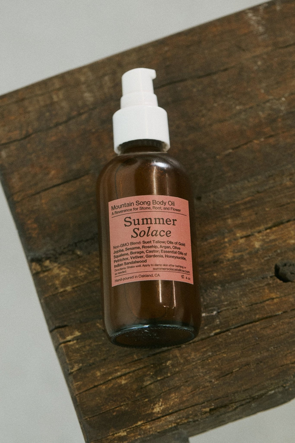 A brown glass bottle of Summer Solace Tallow’s limited edition Mountain Song Body and Hair Oil – Petrichor, Gardenia, Honeysuckle with a white pump sits on rustic wood. Enriched with mountain botanicals and regenerative suet tallow for nourishing care.