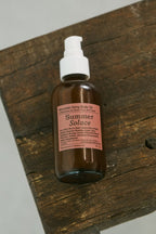 A brown glass bottle of Summer Solace Tallow’s limited edition Mountain Song Body and Hair Oil – Petrichor, Gardenia, Honeysuckle with a white pump sits on rustic wood. Enriched with mountain botanicals and regenerative suet tallow for nourishing care.