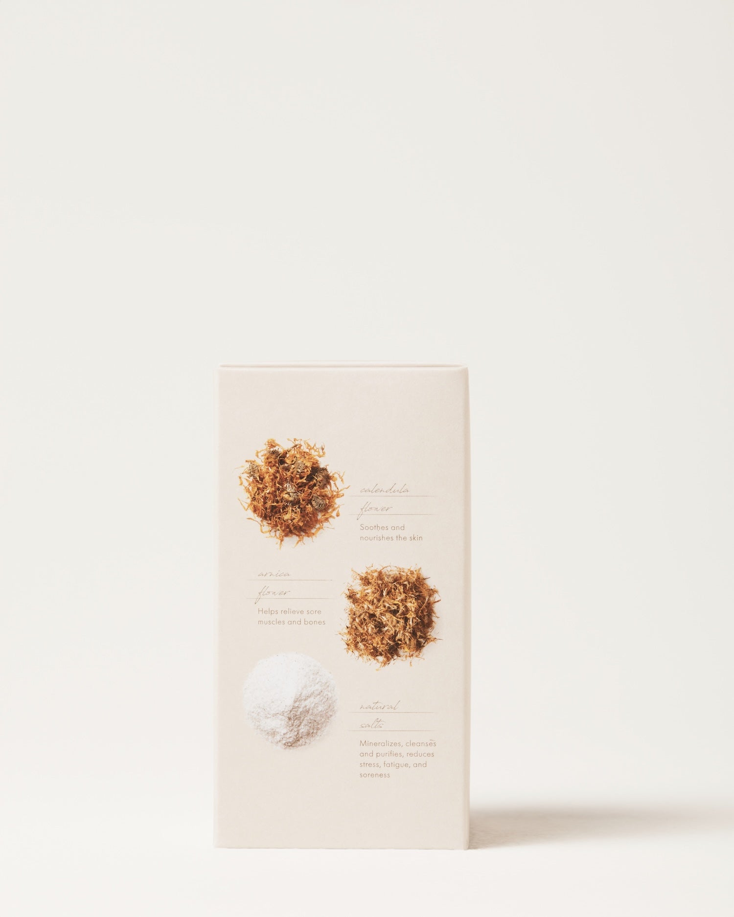 A beige box showcases Surya's Muscle Relief Bath Soak with two piles of dried flowers and a pile of white powder, each with brief labels, evoking a calming Ayurvedic bath experience against a simple, light background.