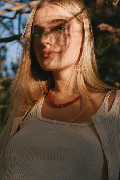 A woman with long blonde hair wears the LA Relaxed Pointelle Square Cami, a white ribbed vintage-inspired top. She stands outdoors, sunlight and tree shadows playing across her face and shoulders.