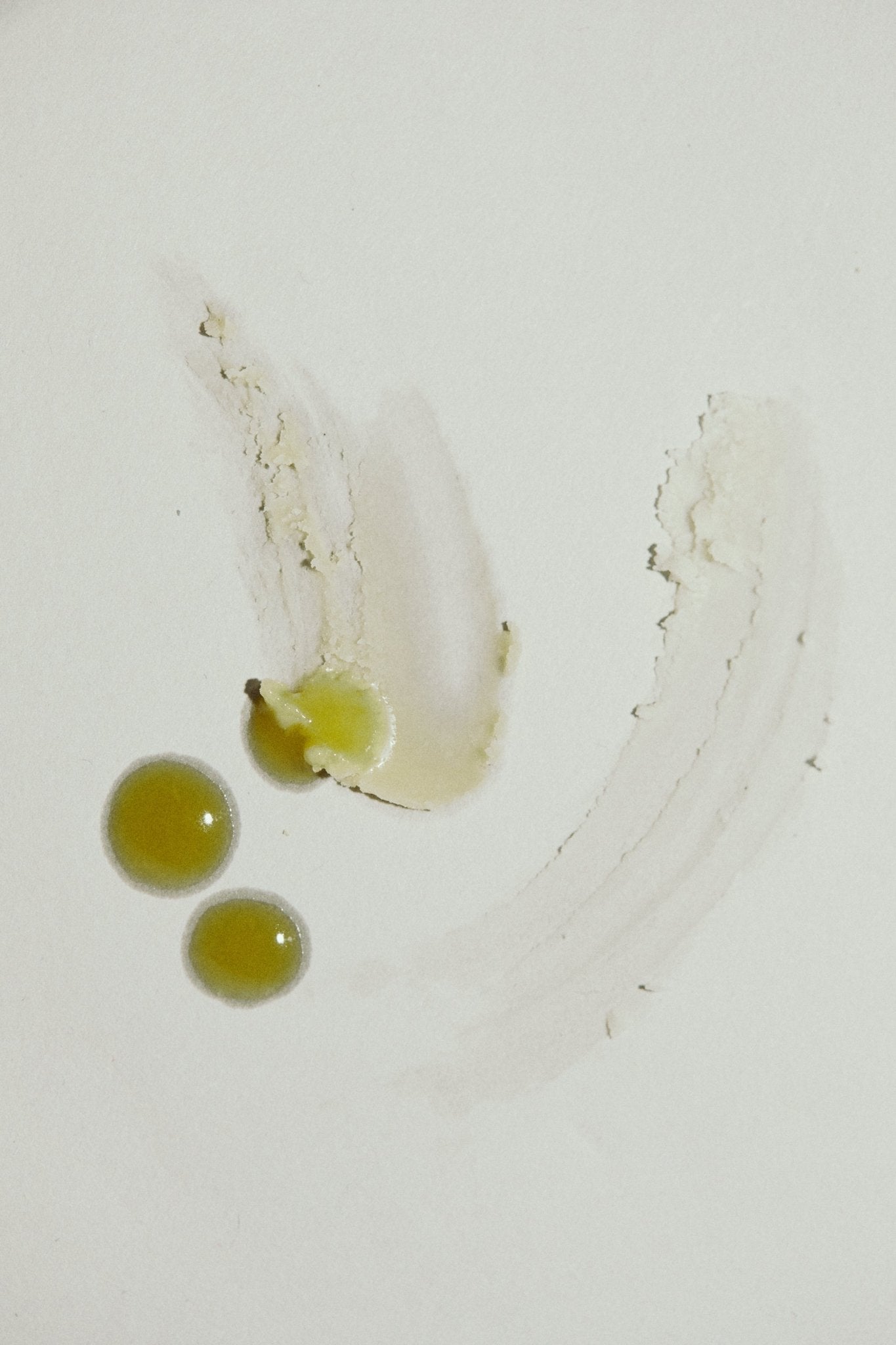 Three olive-green droplets and two beige smudges of Pear Gelato Body Oil – Zinc and Pearl Extract (Limited Edition) by Summer Solace Tallow rest on a white surface, forming an abstract pattern with soft shadows and textured streaks.