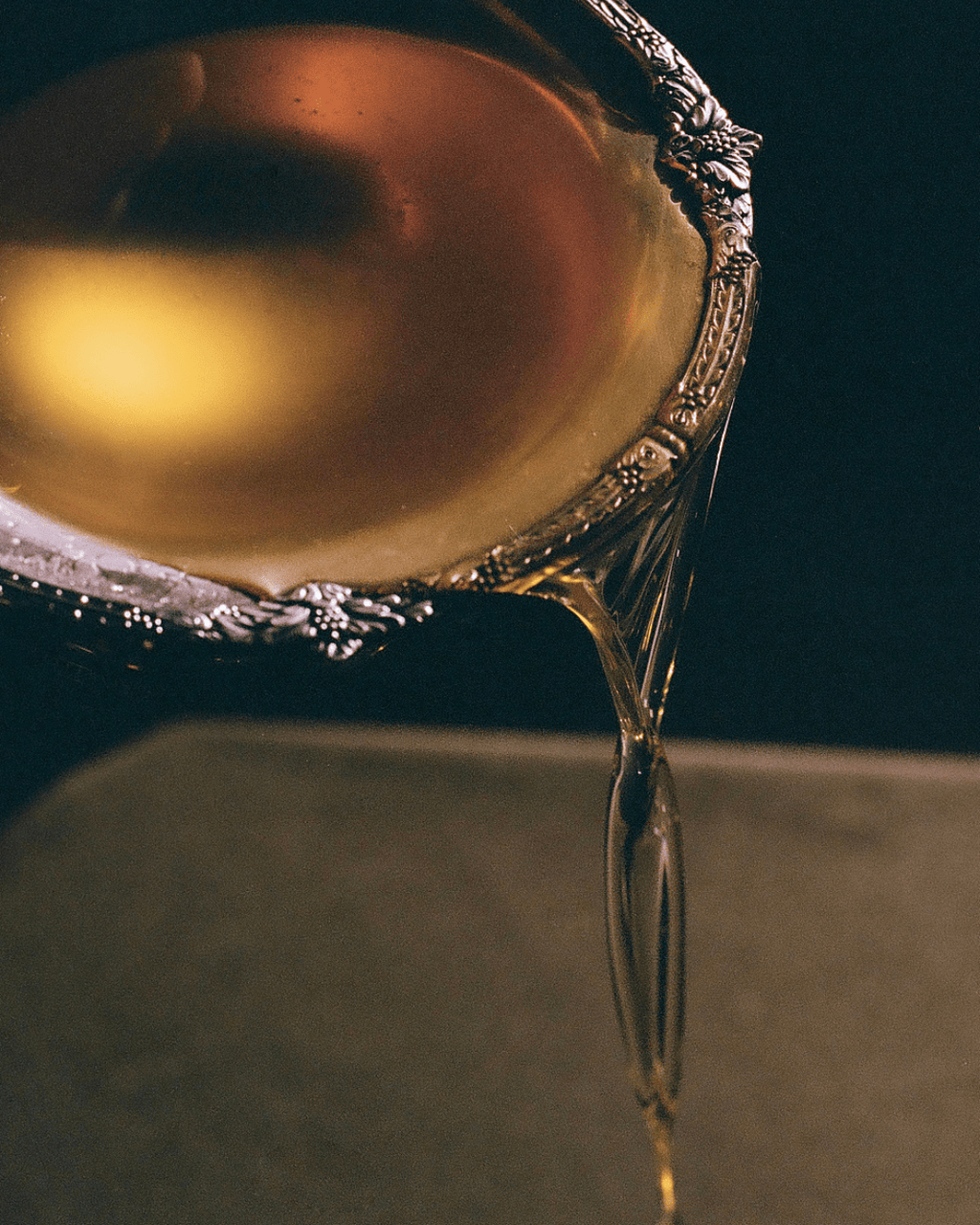 A close-up of golden honey flowing from a silver spoon, evoking the smooth texture of Summer Solace Tallow’s Première Cleansing Oil—Barrier-Respecting Oil Cleanser that gently removes makeup, sunscreen, and daily buildup.
