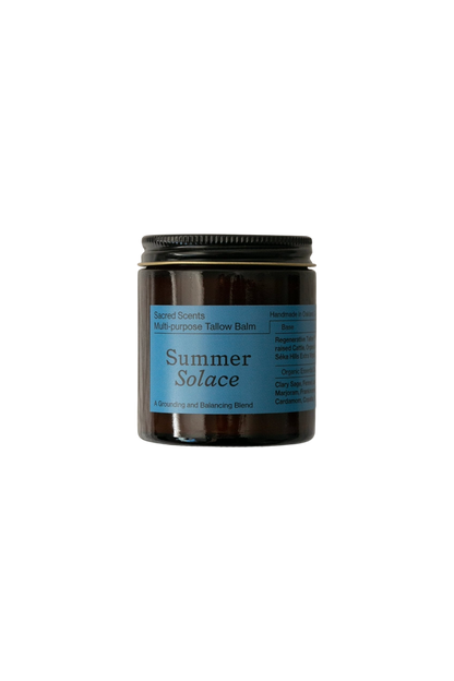 A jar of Summer Solace Tallow's Sacred Scents Spiritual Balm - Regenerative Tallow® is displayed against a black background. The jar features a dark body with a blue label and a black lid. Text on the label includes "Sacred Scents," "Handmade in California," and various ingredients and uses like hormone balancing.