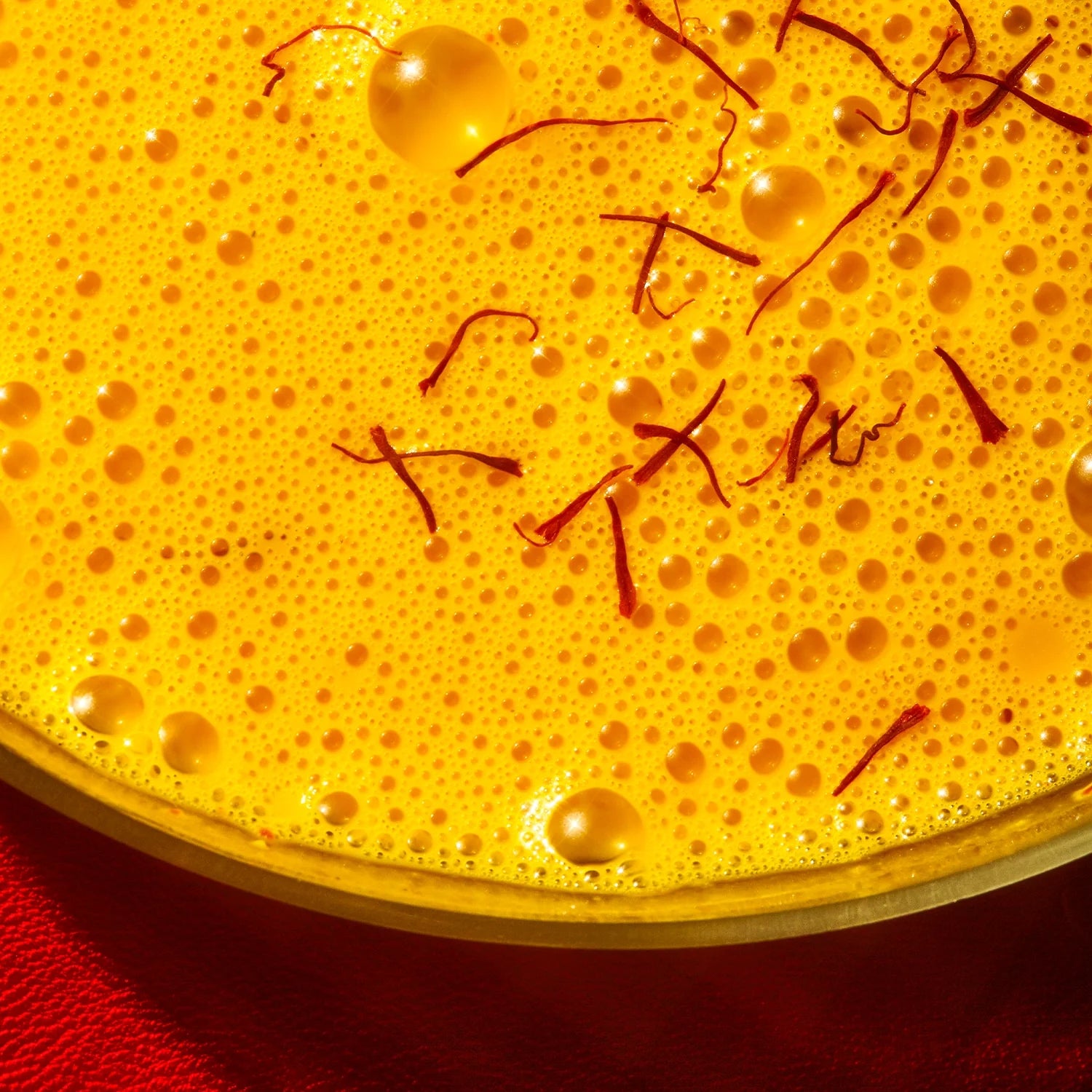 Close-up of The Fullest's Saffron Latte 30-Day Supply—a frothy, caffeine-free yellow drink with saffron strands and bubbles on top, set against a red background for mood support.