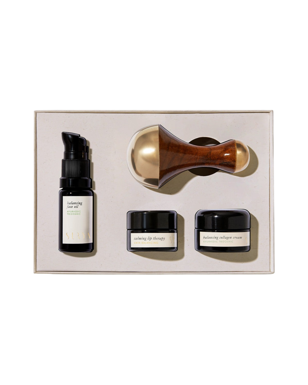 The Surya Skincare Discovery Set includes a serum bottle with pump, two small cream jars, and a Kansa Wand massage tool, all neatly arranged in a beige box.