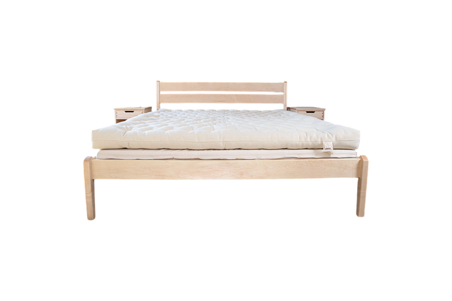 A minimalist wooden bed frame with a slatted headboard is topped with the All Wool Mattress by Shepherd's Dream, featuring a thick, cream-colored natural surface; two small wooden nightstands are placed behind the headboard.