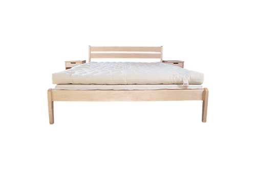 A minimalist wooden bed frame with a slatted headboard is topped with the All Wool Mattress by Shepherd's Dream, featuring a thick, cream-colored natural surface; two small wooden nightstands are placed behind the headboard.
