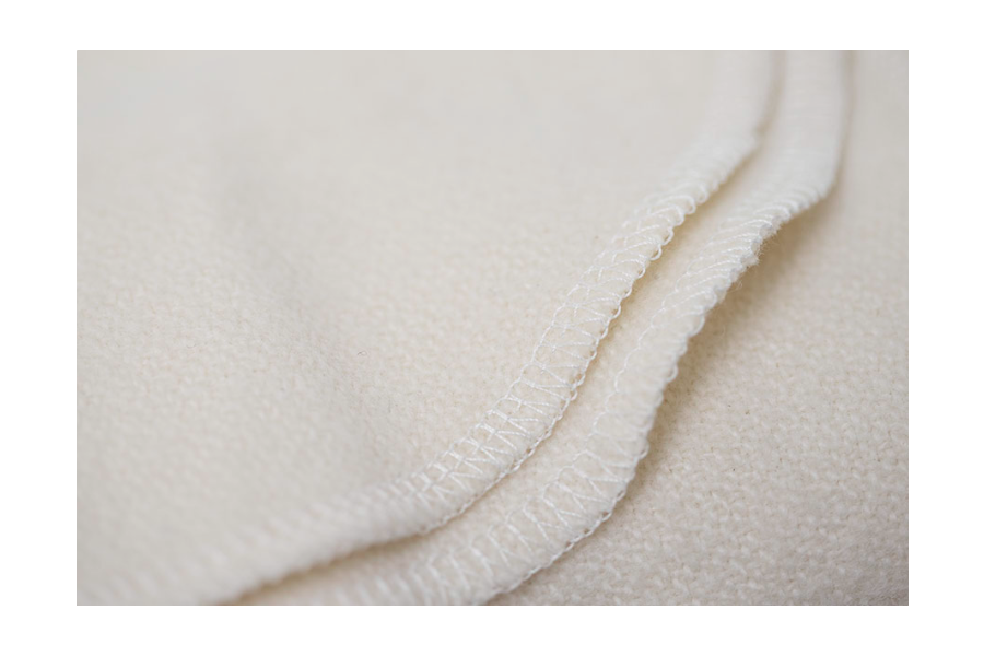 A close-up of the edge of Shepherd’s Dream Organic Merino Wool Blanket shows its soft, cream-colored fabric and detailed hem stitching.