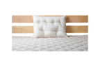 A neatly made bed showcases a light wood headboard with a single white pillow resting against it. The bedspread, quilted in a diamond pattern, rests on the Cascade Latex Mattress by Shepherd's Dream, ensuring restful nights.
