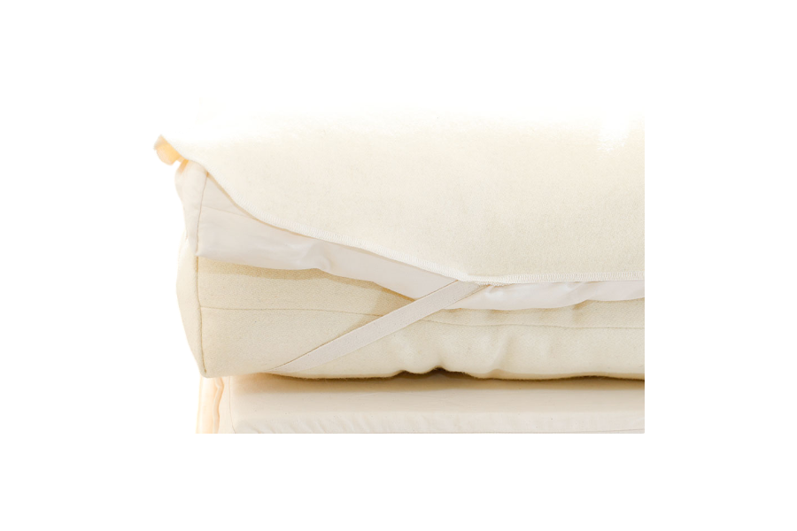 A close-up of the Baile Wool Mattress Protector, cream-colored and washable with elastic straps, folded neatly atop a light foam mattress.