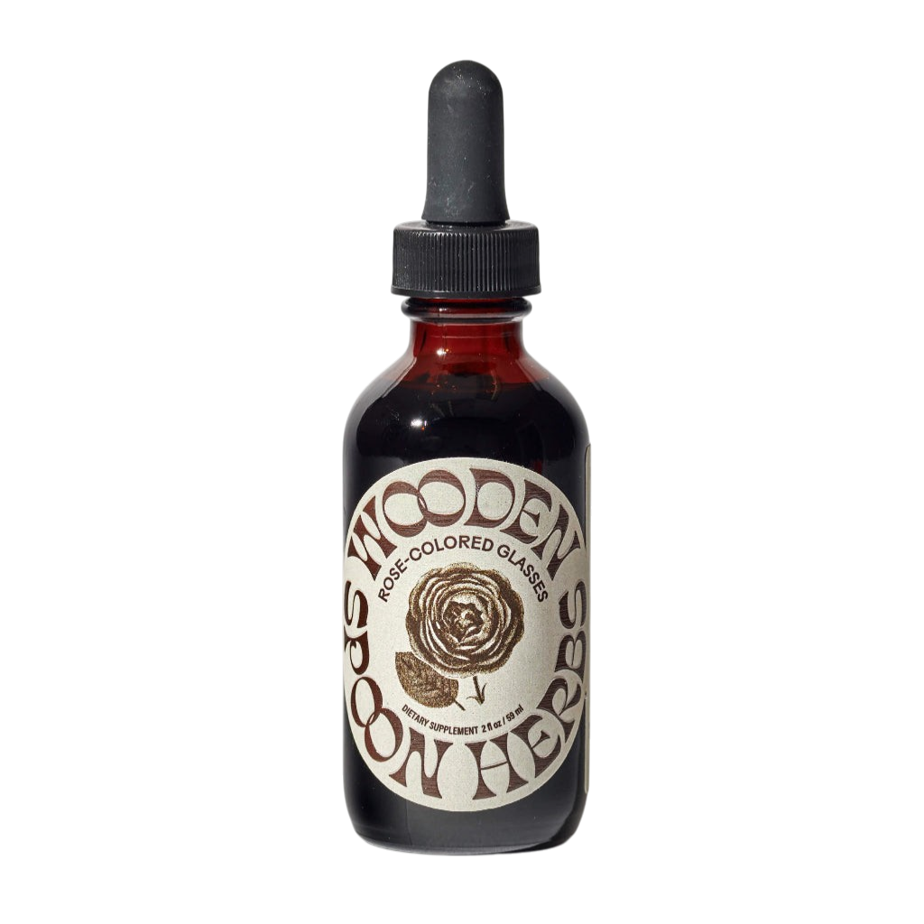 A dark glass dropper bottle labeled "WOODEN SPOON HERBS" with a rose illustration and "Rose-Colored Glasses" contains an herbal tincture for mood support, displayed against a white background.