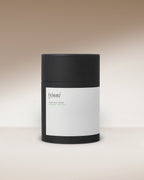 A black cylindrical Surya container with a minimal white label reading “(y)oni Fertility Steam,” designed for yoni fertility steam with Ayurvedic herbs, displayed on a neutral gradient background.