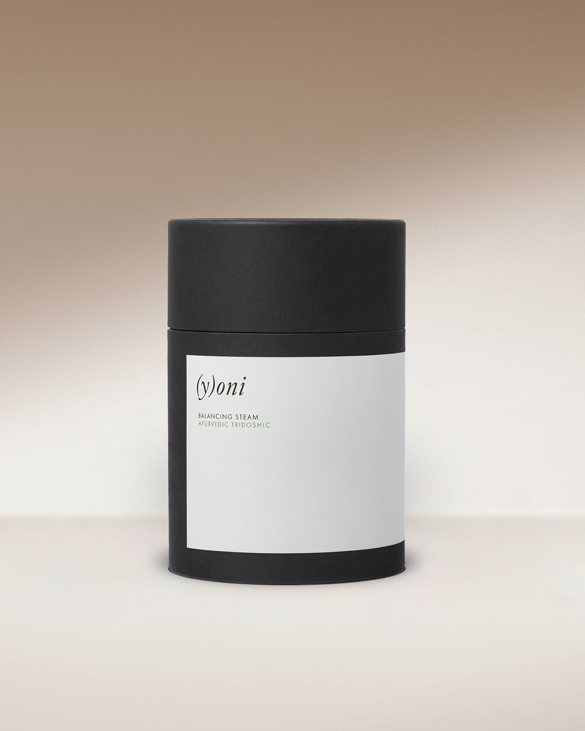A black cylindrical Surya container with a minimal white label reading “(y)oni Fertility Steam,” designed for yoni fertility steam with Ayurvedic herbs, displayed on a neutral gradient background.